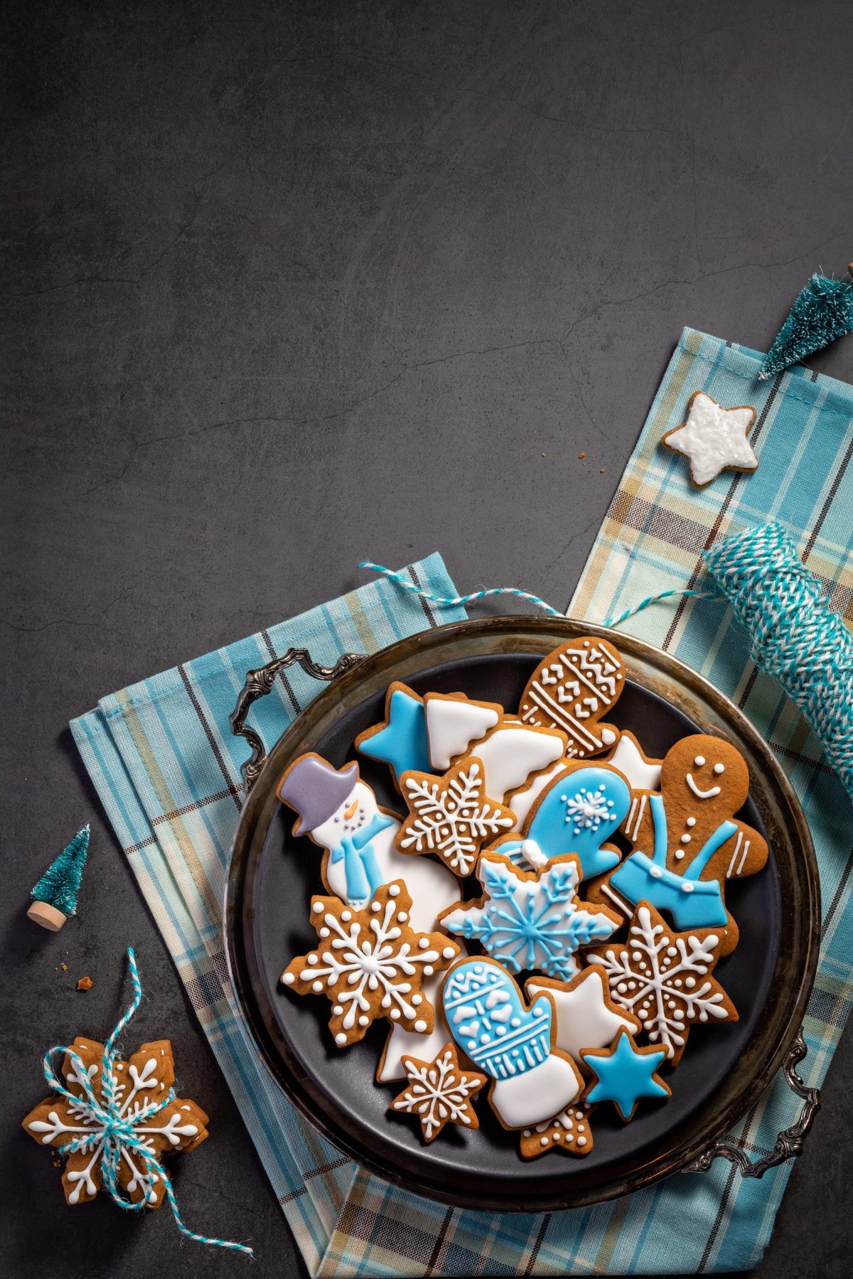 Decorated Blue and White iced gingerbread Christmas cookies on platter on towel with string. Dark Grey background. Top view with copyspace